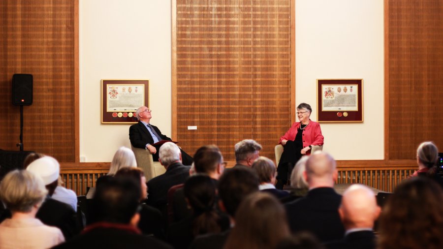 Professor John Naughton and Professor Jane Clarke, the President of Ǻ, sit at the front of the room in front of a crowd of people.