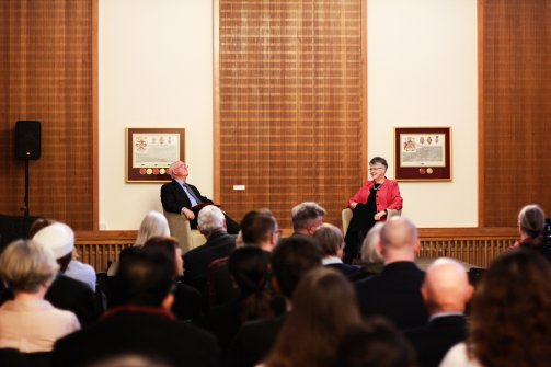 Professor John Naughton and Professor Jane Clarke, the President of Ǻ, sit at the front of the room in front of a crowd of people.